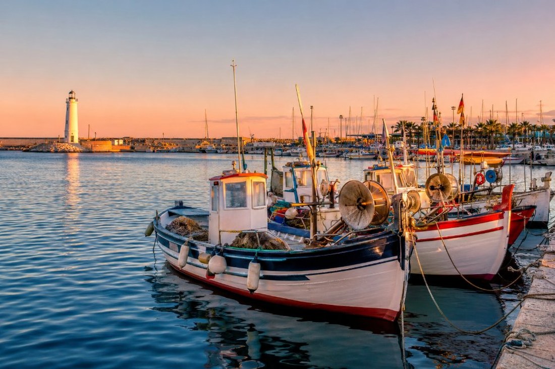 Puerto pesquero de Cambrils con barcas tradicionales amarradas y el faro al fondo en la hora dorada
