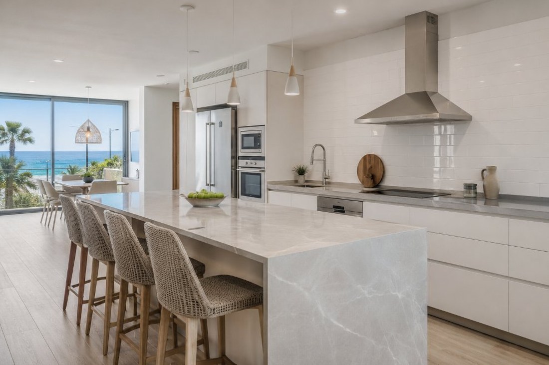 Cocina abierta de un apartamento de Cambrils con isla de encimera clara y vista al mar a través del ventanal