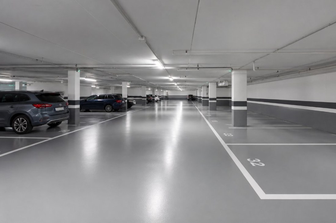 Garaje comunitario de un edificio de pisos con pavimento epoxi gris y plazas numeradas con líneas blancas