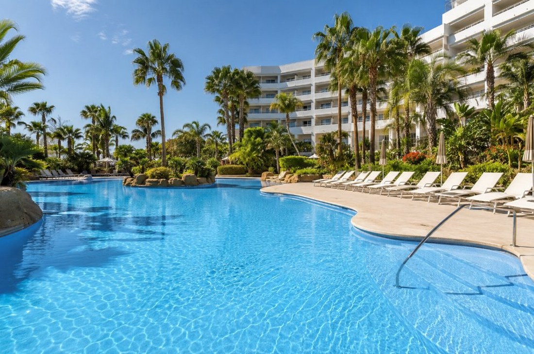 Piscina de hotel resort en Salou de forma libre con agua azul, palmeras y hamacas blancas en el solárium