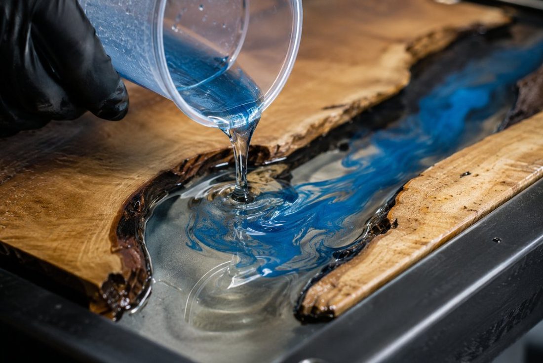 Proceso de vertido de resina epoxi pigmentada en azul sobre una tabla de madera durante la fabricación de una mesa río