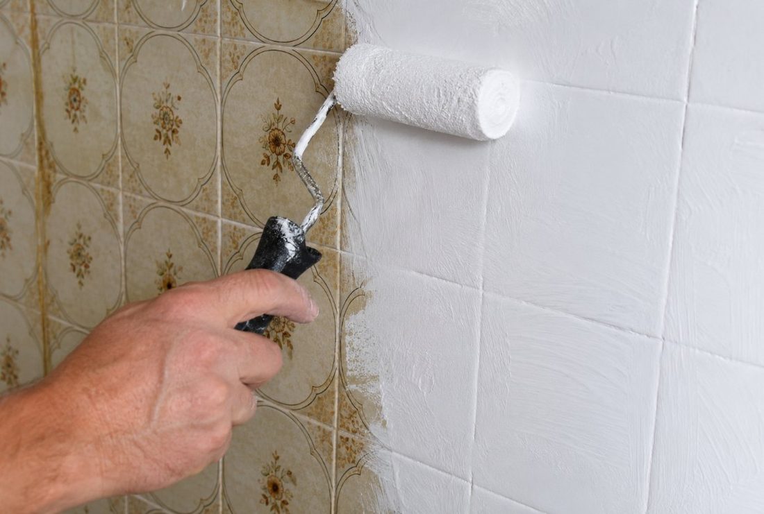 Aplicación de esmalte epoxi blanco con rodillo de espuma sobre azulejos antiguos durante una renovación exprés